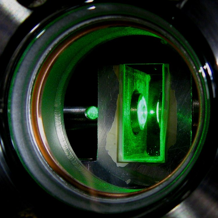 The optical trap and the speed of a Brownian particle. The focused green laser holds a Brownian particle. The scattering from the particle gives information about the instantaneous position of the particle and it is recorded 75 million times per second using a novel photodetector. The position increments tell show the researchers the instantaneous speed of the particle.