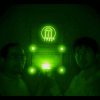 Shedding light in the dark. Zhengwei Pan and Feng Liu stand in a darkened room, using nothing but their recently invented ceramic discs that emit infrared light as a source of illumination. The image was taken using a digital camera with a night vision monocular. Their phosphorescent material was also mixed into the paint that was used to create the UGA logo behind them. There is no other source of illumination in the room; without the aid of a night vision device, the image would be completely dark.
