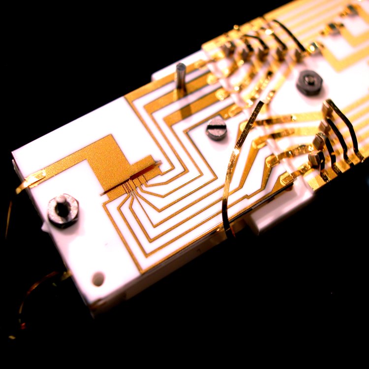 The heart of the quantum computer. This is where the ions are physically stored and processed, surrounded by lasers, electronics and vacuum systems. Tiny trap segments located at the end of this bar confine and control the ions. Quantum information processing and cooling are done by shining laser beams onto the ions.